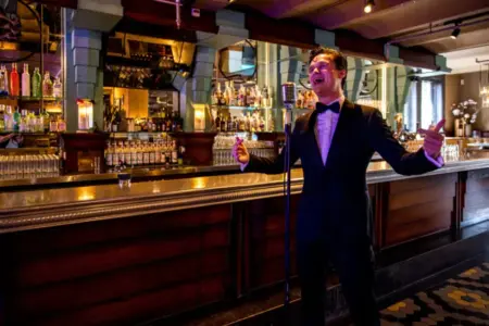 Dennis van Aarssen steht in einem Anzug in einer beleuchteten Bar an einem Mikrofon und singt.