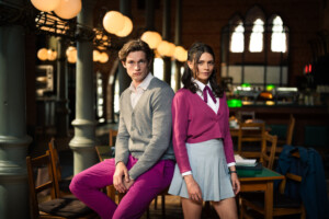 James Beaufort (Damian Hardung) und Ruby Bell (Harriet Herbig-Matten) sitzen in Schuluniform im Klassenzimmer der Maxton Hall auf einem Tisch und schauen zur Kamera. „Maxton Hall“ kann bei Amazon Prime Video gestreamt werden.