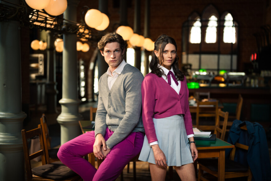 James Beaufort (Damian Hardung) und Ruby Bell (Harriet Herbig-Matten) sitzen in Schuluniform im Klassenzimmer der Maxton Hall auf einem Tisch und schauen zur Kamera. „Maxton Hall“ kann bei Amazon Prime Video gestreamt werden.