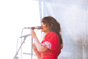 Sängerin Bellefolie steht auf einer Bühne und singt in das Mikrofon während sie in die Ferne schaut.