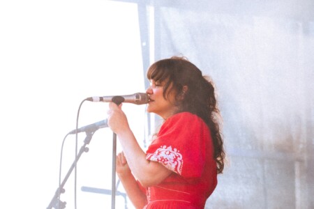 Sängerin Bellefolie steht auf einer Bühne und singt in das Mikrofon während sie in die Ferne schaut.