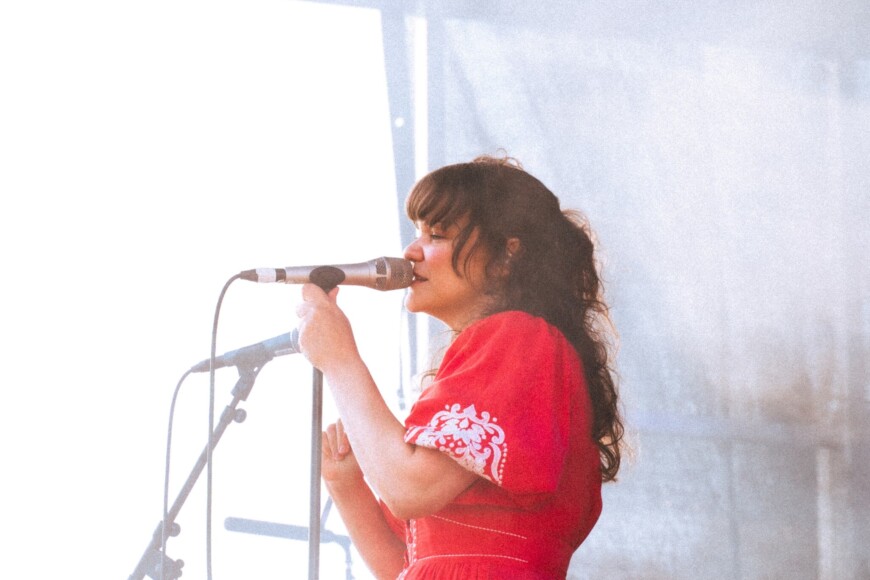 Sängerin Bellefolie steht auf einer Bühne und singt in das Mikrofon während sie in die Ferne schaut.