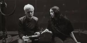 James Cameron sitzt neben Billie Eilish in einer leeren Arena, sie diskutieren über den Film.