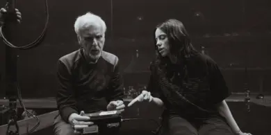 James Cameron sitzt neben Billie Eilish in einer leeren Arena, sie diskutieren über den Film.
