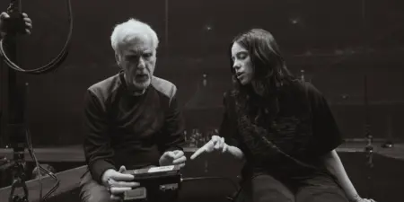 James Cameron sitzt neben Billie Eilish in einer leeren Arena, sie diskutieren über den Film.