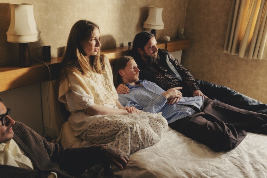 Die band Dry Cleaning liegt auf einem Bett und schaut aus dem Fenster.