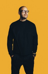 Schiller, der it schwarzer Kleidung vor einen gelben Hintergrund steht