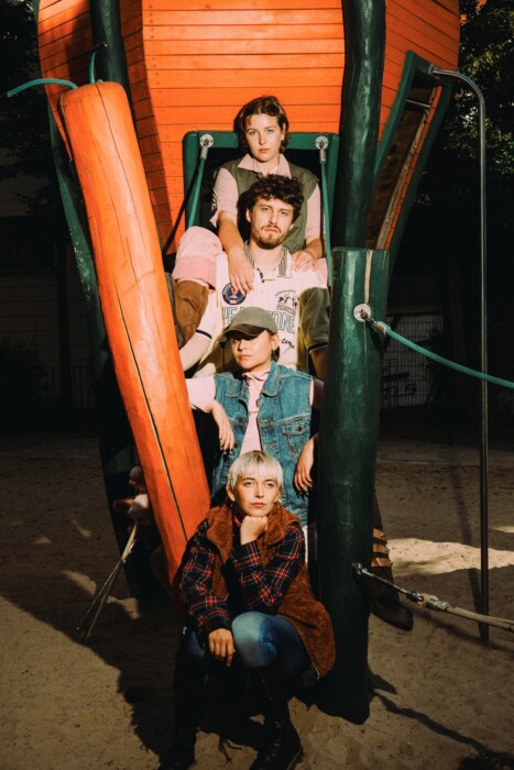 Die Band Remote Bondage sitzt hintereinander auf einer Rutsche auf einem Spielplatz.