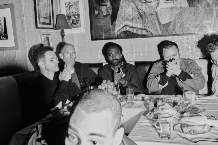 Die Bandmitglieder der Bleachers sitzen versammelt um einen gedeckten Tisch.