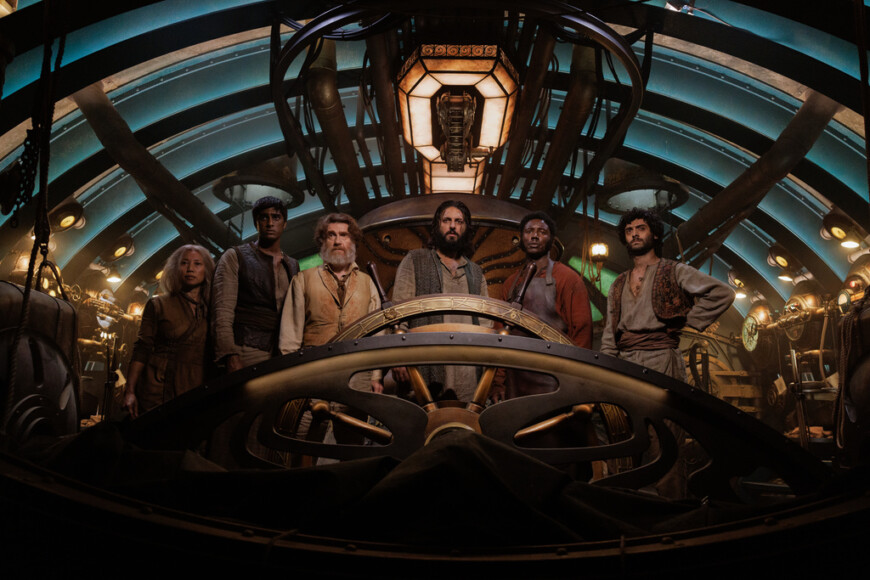 "Nautilus - Anahata": Suyin (Ling Cooper Tang), Ranbir (Ashan Kumar), Benoit (Thierry Frémont), Nemo (Shazad Latif), Boniface (Pacharo Mzembe) und Turan (Arlo Green) stehen nebeneinander im Innern eines U-Boots hinter einem großen Steuerrad.