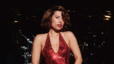 Raye steht in einem Abendkleid vor Instrumenten und schaut in die Kamera.