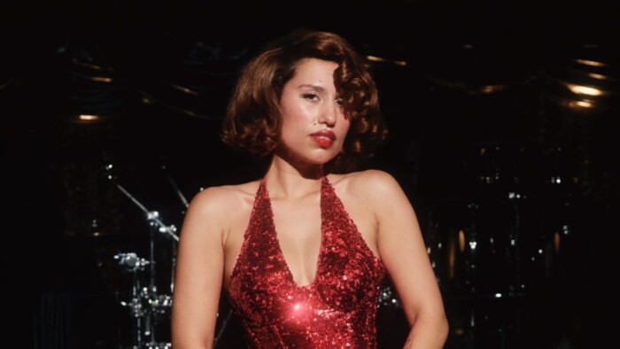 Raye steht in einem Abendkleid vor Instrumenten und schaut in die Kamera.