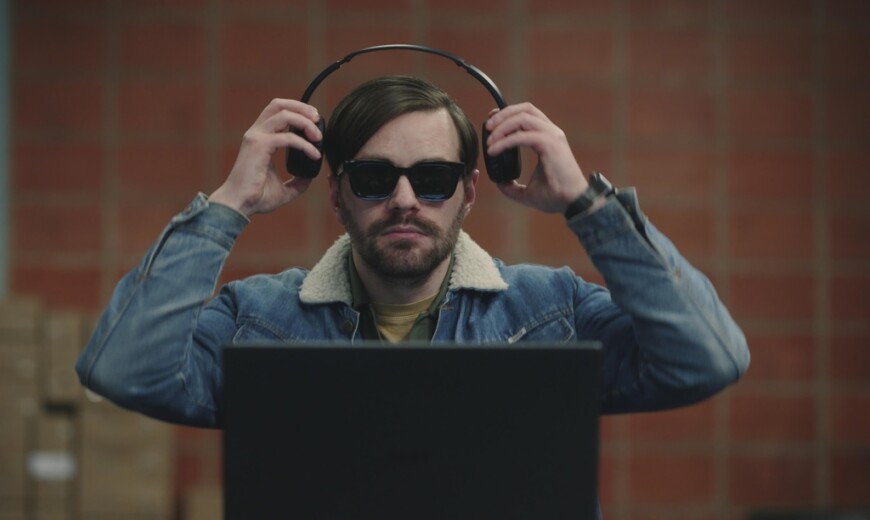 Roman Mertens (Bart Kelchtermans) sitzt in einem Raum vor einem aufgeklappten Laptop. Er trägt eine dunkle Brille und setzt sich gerade Kopfhörer auf. Roman Mertens (Bart Kelchtermans) beginnt bei der rotterdamer Polizei zu arbeiten und hilft ihnen Abhöraufnahmen zu analysieren. „Blind Sherlock“ läuft im Zweiten und kann in der ZDF-Mediathek gestreamt werden.