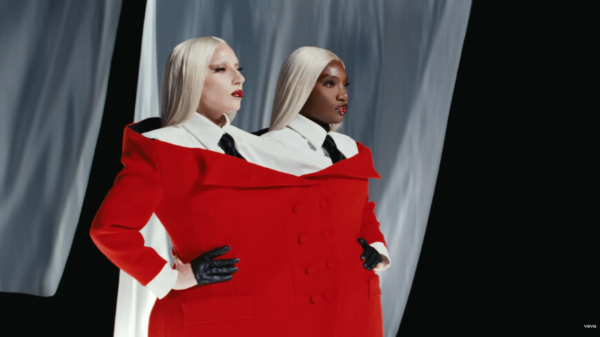 Sängerinnen Lady Gaga und Doechii stehen in einem großen roten Mantel auf einem Laufsteg.