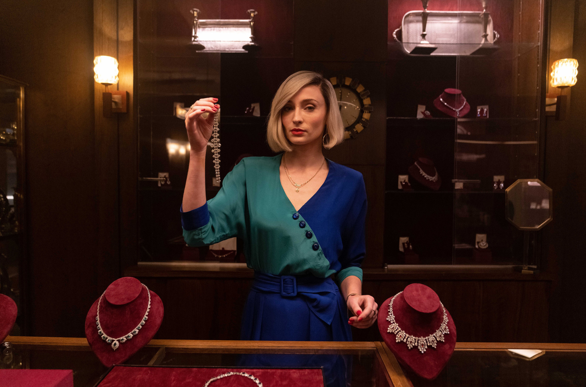 Joan steht im eleganten blau-grünen Outfit im Juweliergeschäft