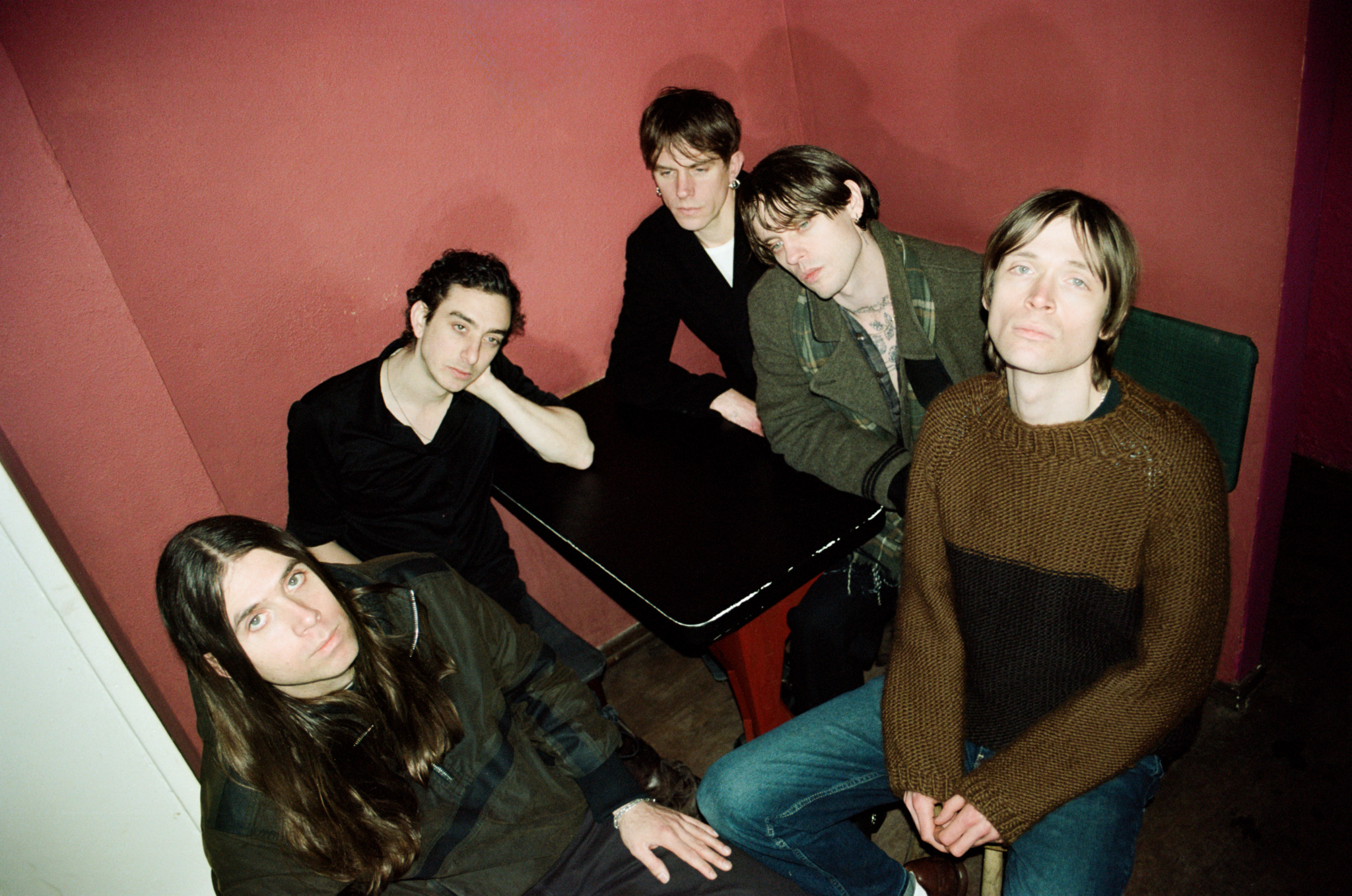 Die Band Iceage sitzt auf Stühlen vor einer orangenen Wand.