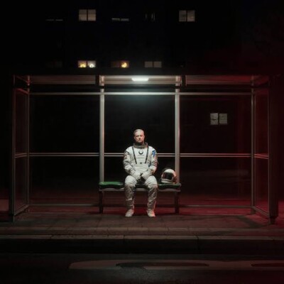 Cover von „Drama endet nie“: Fatoni sitzt nachts im Raumanzug in einem Bushaltestellenhäuschen.