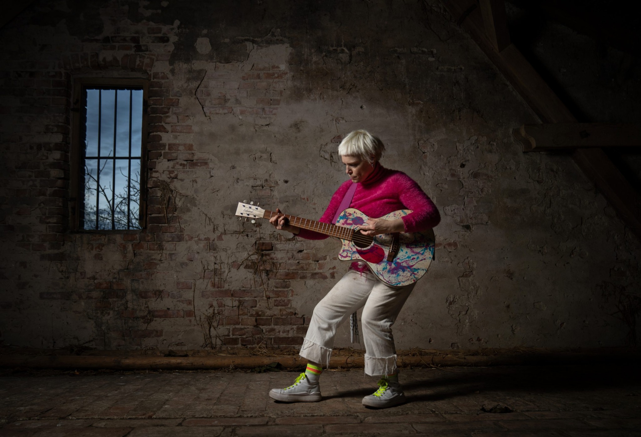 Wallis Bird spielt Gitarre vor einer dunklen Hauswand mit kleinem Fenster.
