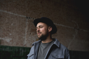 Max Mutzke trägt eine graue Jacke und einen der schwarzen Hüte, die für ihn charakteristisch sind.