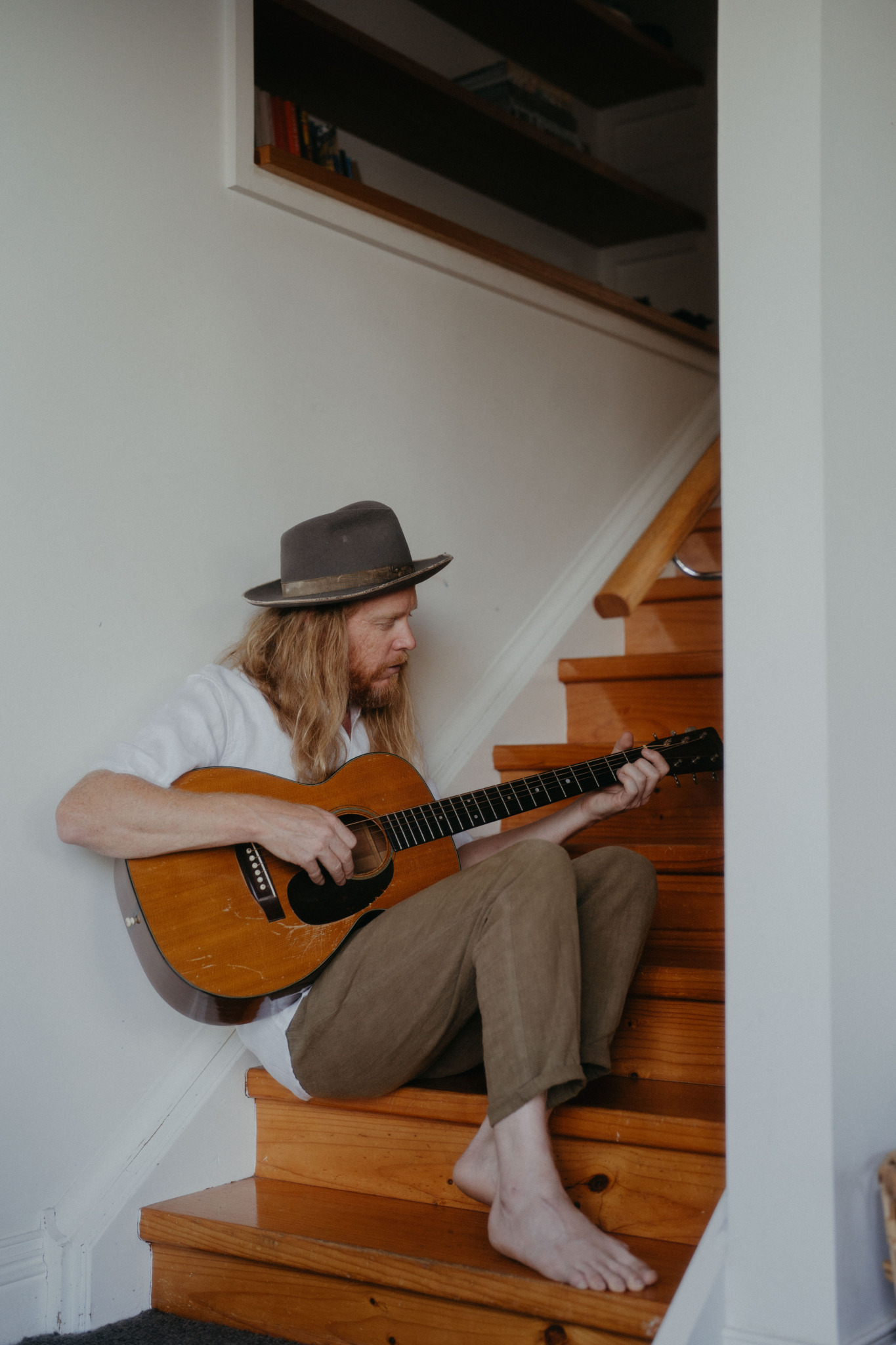 Stu Larsen sitzt drinnen auf einer Treppe und spielt Gitarre.