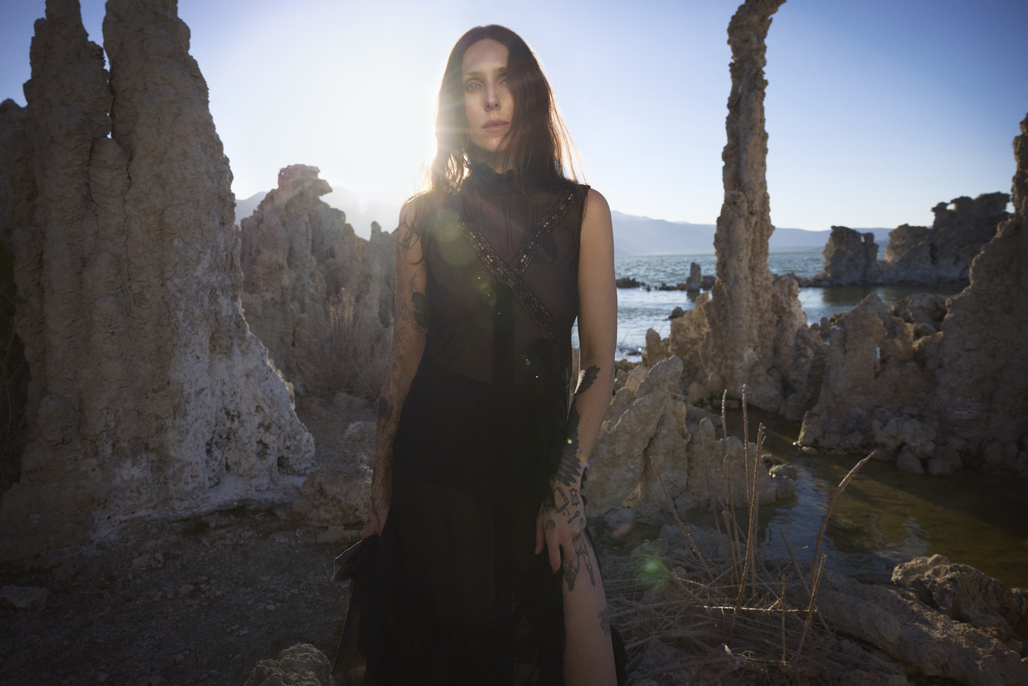 Chelsea Wolfe steht in einem dunklen Kleid in einer felsigen Landschaft, durchzogen von Bächen.