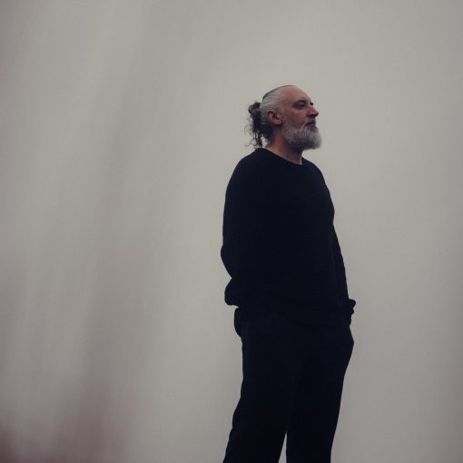 Fink (Fin Greenall) steht mit den Händen in der Tasche gedankenverloren vor einem diesigen Hintergrund