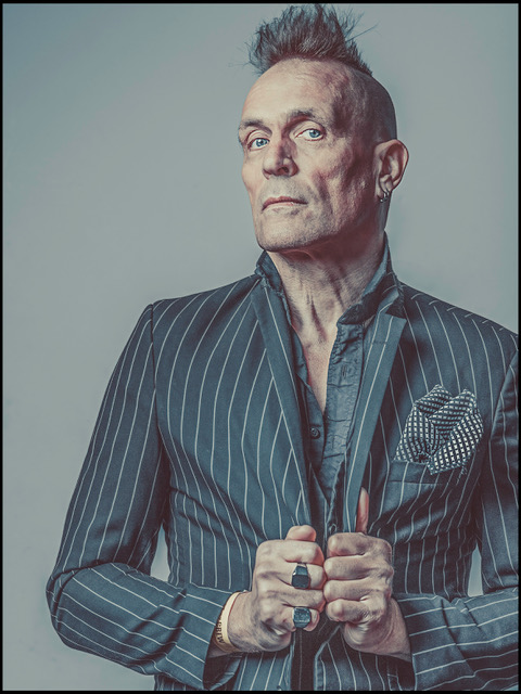 John Robb wird bei „A Life without Punk“ auftreten. Hier trägt er ein gestreiftes Jacket, das er am Revere festhält.