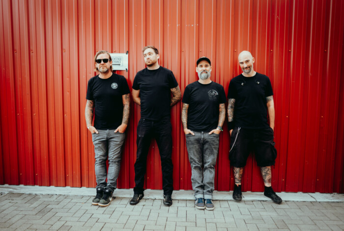 Die Band Massendefekt steht vor einer roten Wand und schaut in die Kamera.