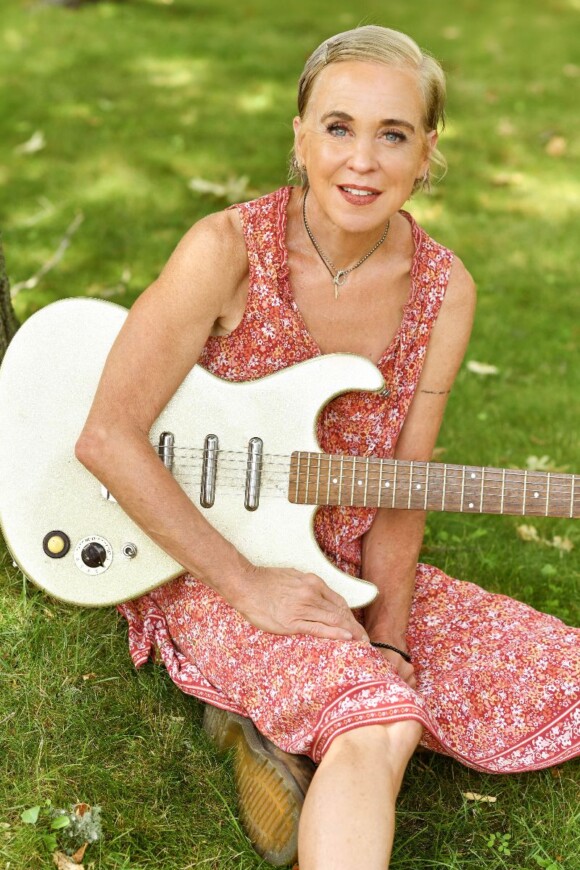 Kristin Hersh sitzt mit Gitarre auf dem einer Wiese